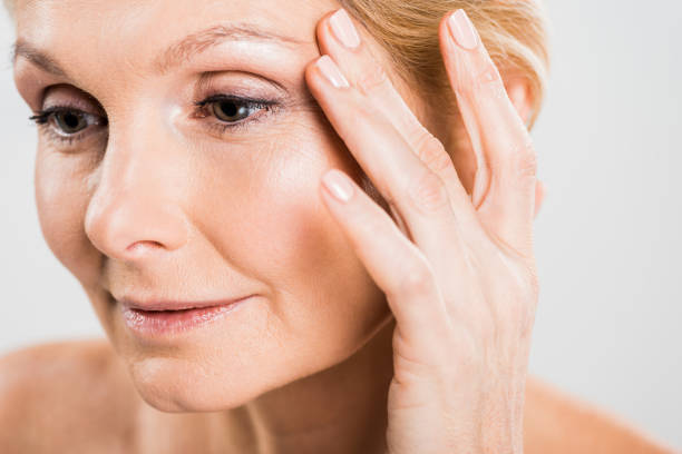 beautiful mature woman touching her face and looking away isolated on grey